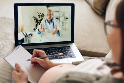 Paciente grávida sendo atendida por médico via telemedicina com notebook