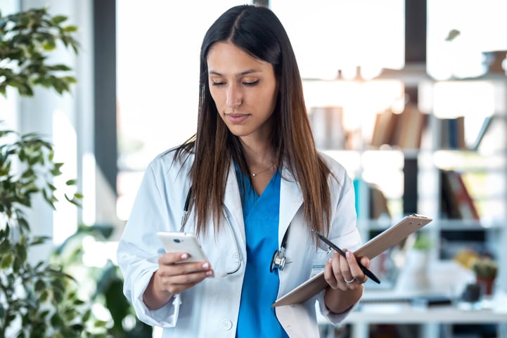 Médica com celular em uma mão e uma prancheta com caneta em outra, aprendendo a lidar com pacientes que desmarcam em cima da hora