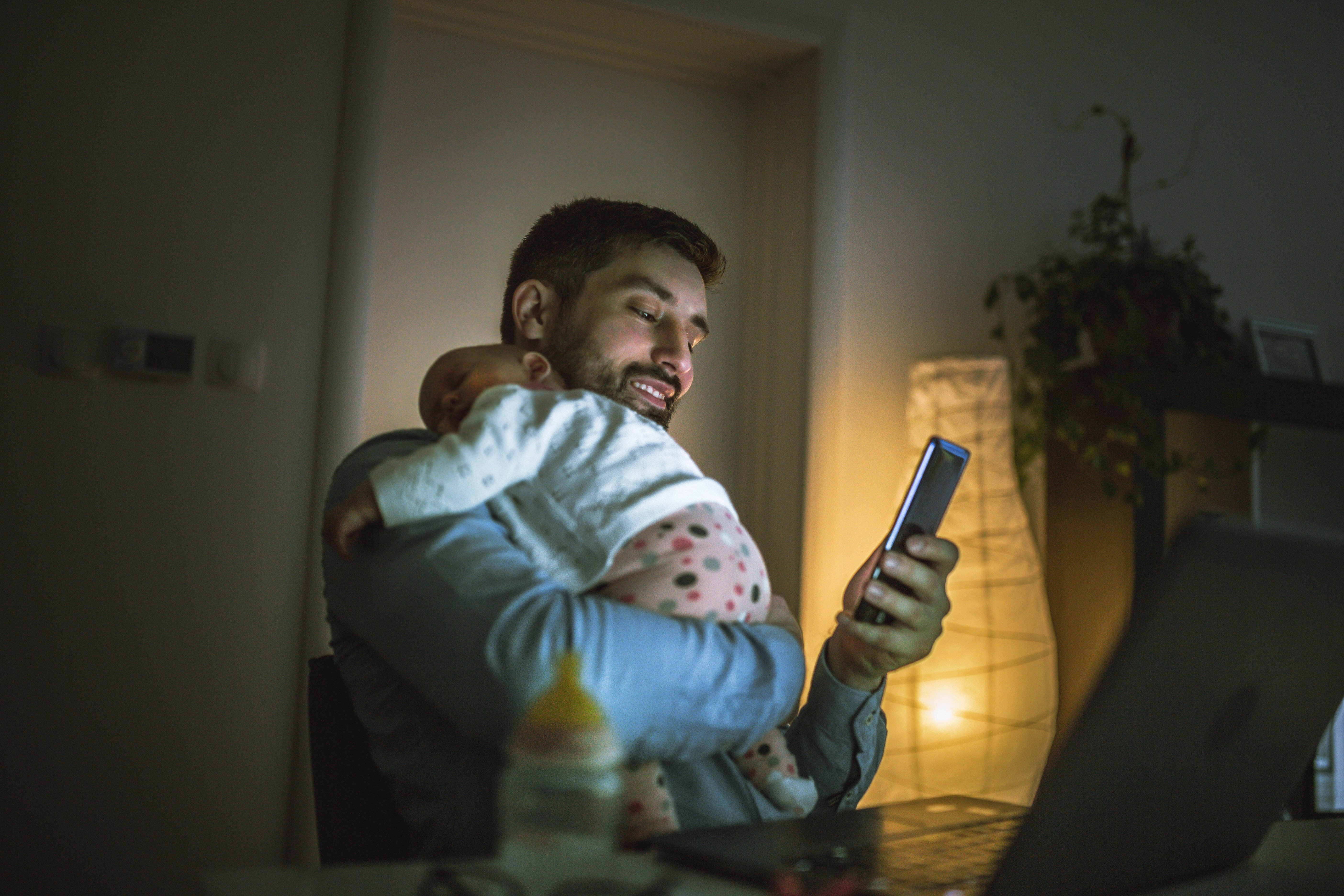 Pai com bebê no colo realizando agendamento de consultas online à noite