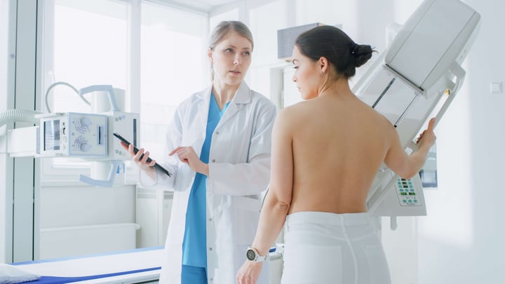 In-the-Hospital,-Female-Patient-Listens-to-Mammography-Technologist--Doctor-Uses-Tablet-Computer,-Explains-Importance-of-Breast-Cancer-Prevention.-Mammography-Procedure.-996271574_5120x2880